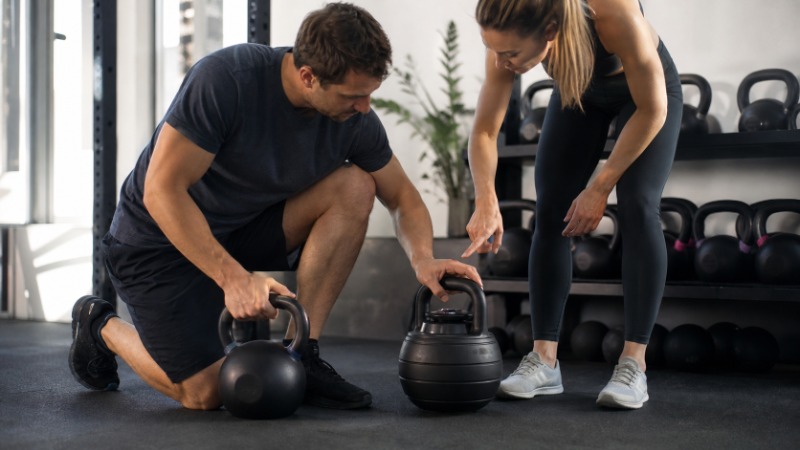Řada litinových kettlebellů různých vah srovnaná na podlaze domácí posilovny